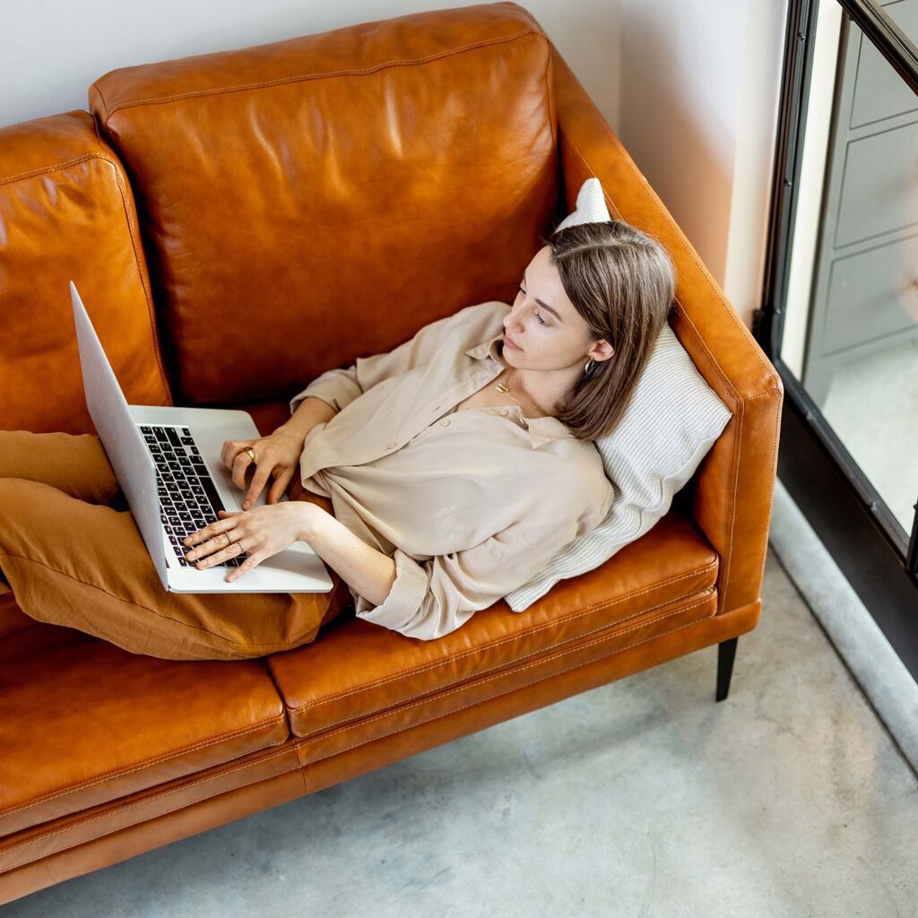 woman working on laptop and lying on sofa 34PDYDR 2